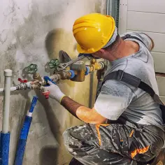 Hydraulik w żółtym kasku reguluje zawory. Zastanawiasz się, ile kosztuje punkt hydrauliczny?