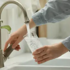 Ręce nalewają wodę do szklanki z kranu. Kto odpowiada za przyłącze wodociągowe, gdy woda płynie tak czysta?