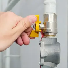 Dłoń przekręca żółty zawór, pokazując, jak wyłączyć gaz w mieszkaniu. Bezpieczeństwo przede wszystkim!