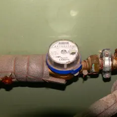 Hydraulik naprawia zawór przed wodomierzem. Rura jest izolowana, a zawór wygląda na skorodowany.
