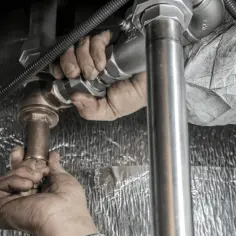 Dłonie hydraulika pracują nad połączeniem rur. Zastanawiasz się, czym rozpuścić kamień w rurach?