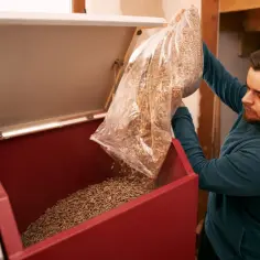 Mężczyzna wsypuje pellet do kotła. Zastanawiasz się, ile kosztuje brykiet? To ekologiczne paliwo jest coraz popularniejsze.