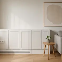 Elegancka zabudowa kryje grzejnik, pokazując, jak ukryć rury w domu. Minimalistyczny salon z sofą i obrazem.