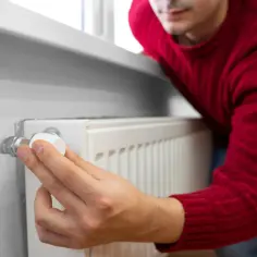 Mężczyzna reguluje termostat grzejnika, próbując wyeliminować stuki w rurach centralnego ogrzewania.