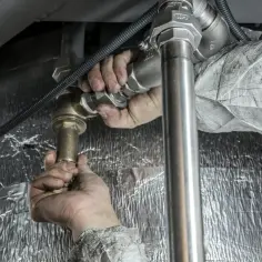 Ręce majsterkowicza łączą rury, ucząc się jak zostać hydraulikiem bez szkoły.