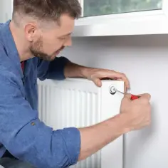 Mężczyzna używa śrubokręta, by odpowietrzyć grzejnik w domu. To prosty sposób na pozbycie się powietrza z instalacji CO.