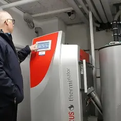 Mężczyzna sprawdza panel sterowania kotła na pellet. Dowiedz się, ile kosztuje piec na pellet z montażem i jakie są jego zalety.