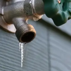 Sople lodu zwisają z kranu, pokazując, przy jakiej temperaturze zamarza woda w rurach.