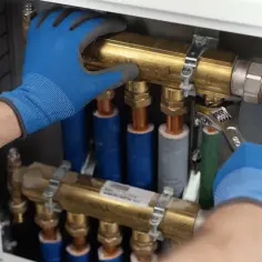 Ręce w niebieskich rękawiczkach montują instalację hydrauliczną, używając klucza.