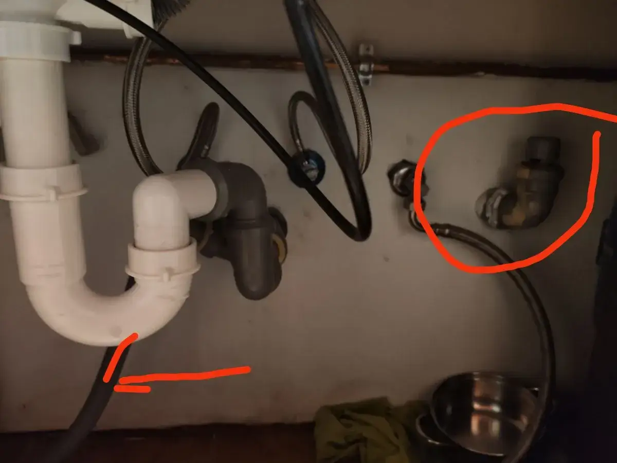 Pod zlewem widać instalację hydrauliczną. Woda ze zlewu cofa się do zmywarki, co sugeruje problem z odpływem.