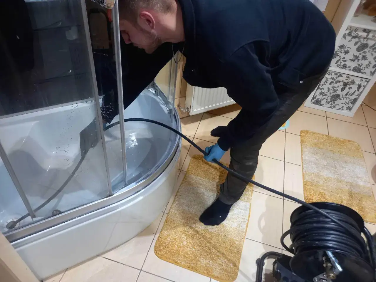 Fachowiec z pogotowia kanalizacyjnego używa sprzętu do udrażniania rur w kabinie prysznicowej.