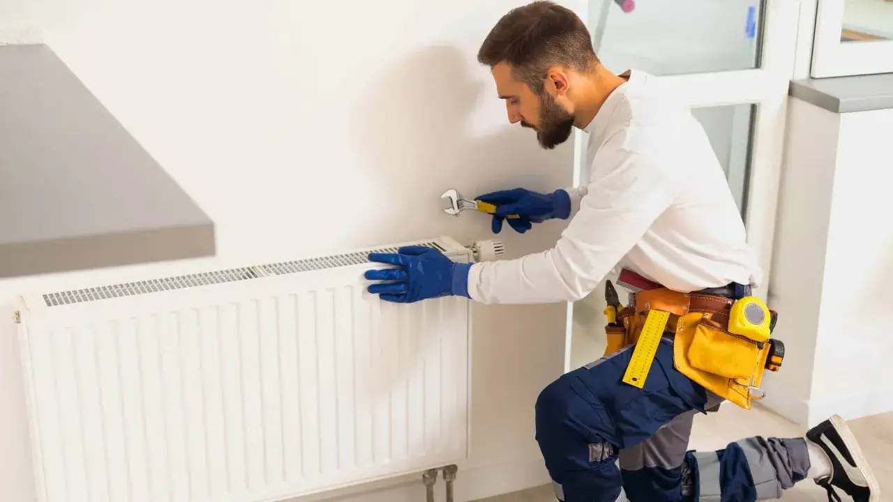Instalator w niebieskich rękawiczkach reguluje odpowietrznik, gdy kaloryfer jest zapowietrzony.