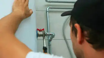 Fachowiec z Gdańska, dobry hydraulik, dokręca zawór przy bojlerze.